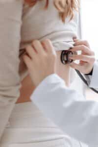 a person in white long sleeves checking up the back of the patient using stethoscope